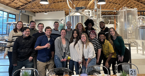 group of 16 people standing in front of beer making machine